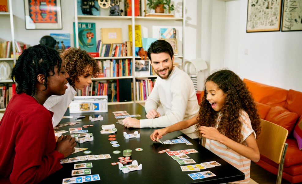 Une famille joue au jeu de société 7 wonders architects autour d'une table.