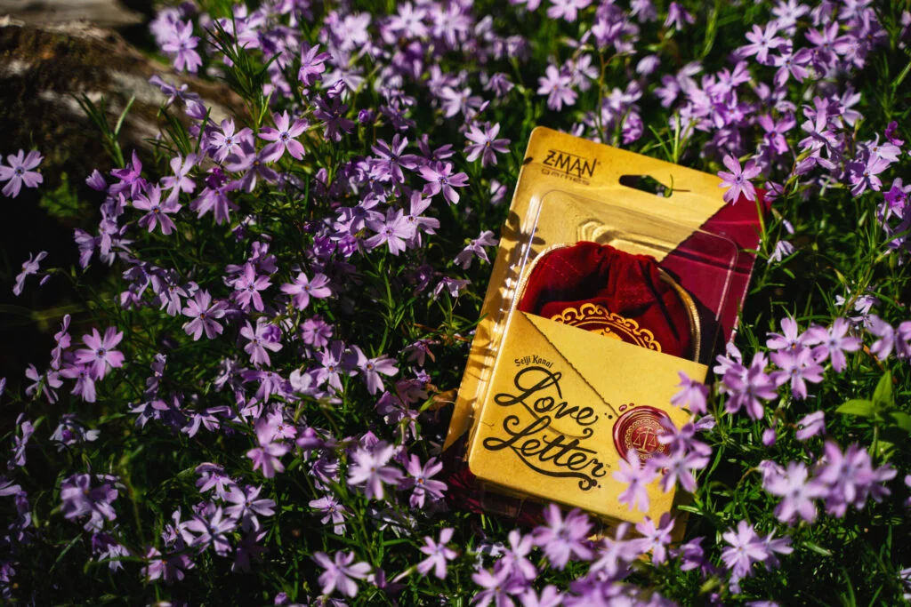 Boîte jeu de société Love Letter posée dans des fleurs