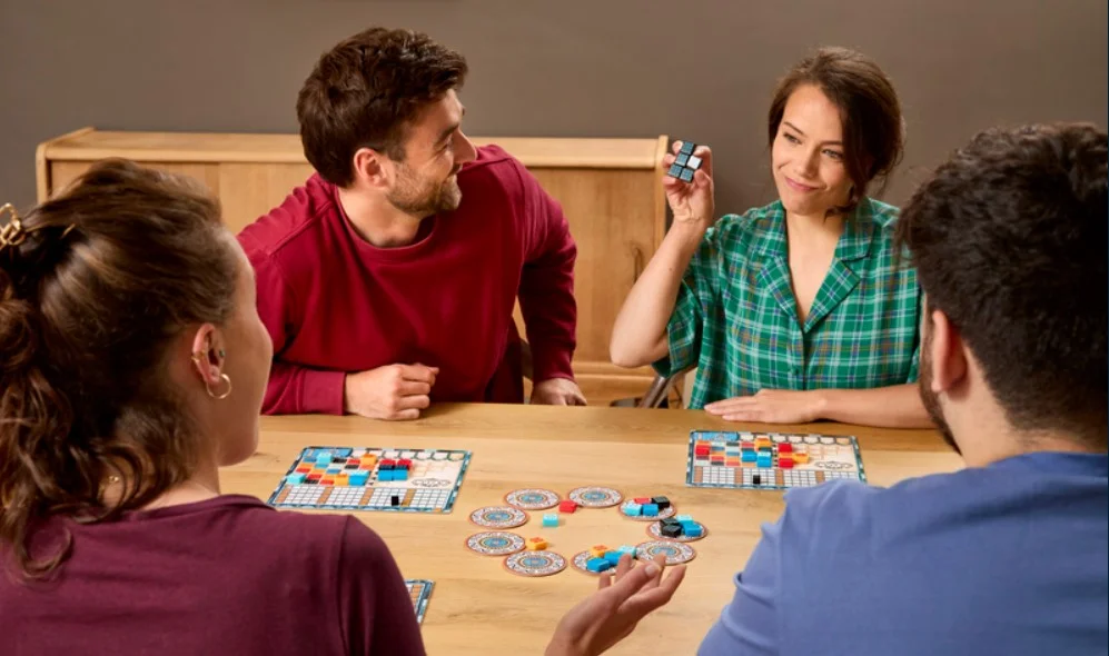 Joueurs jouant à Azul autour d'une table, une femme montre ses mosaïques avec un air satisfait
